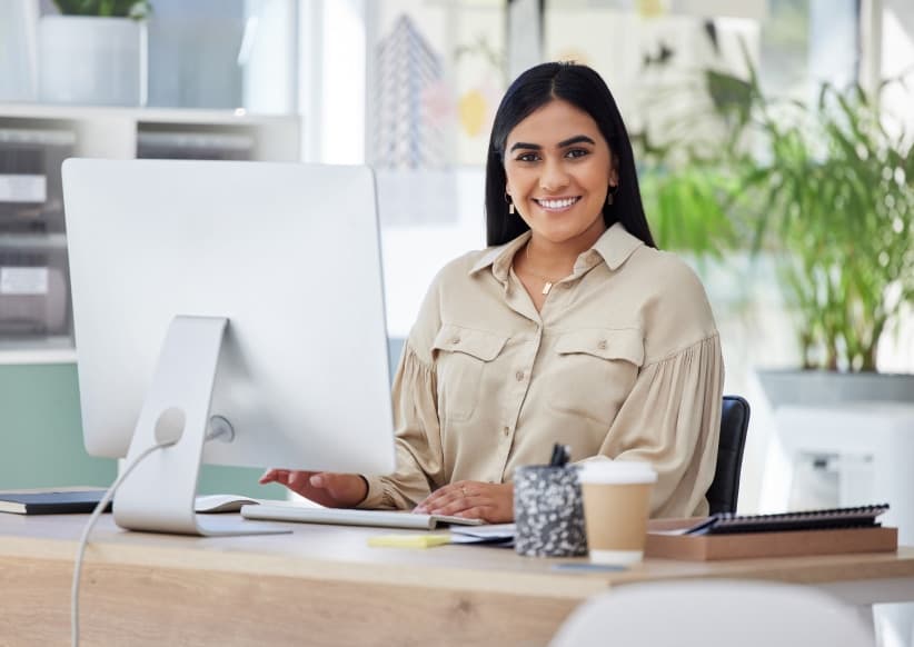 woman on a beige shirt at her desk smiling